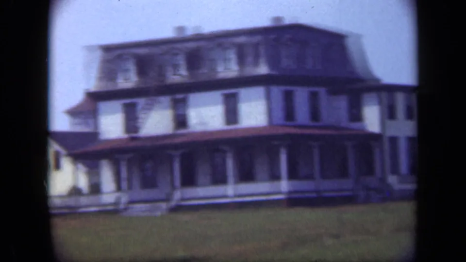 1948 Long Island footage frame showing a long multi-story house or lodging-style building with a broad porch and lawn.