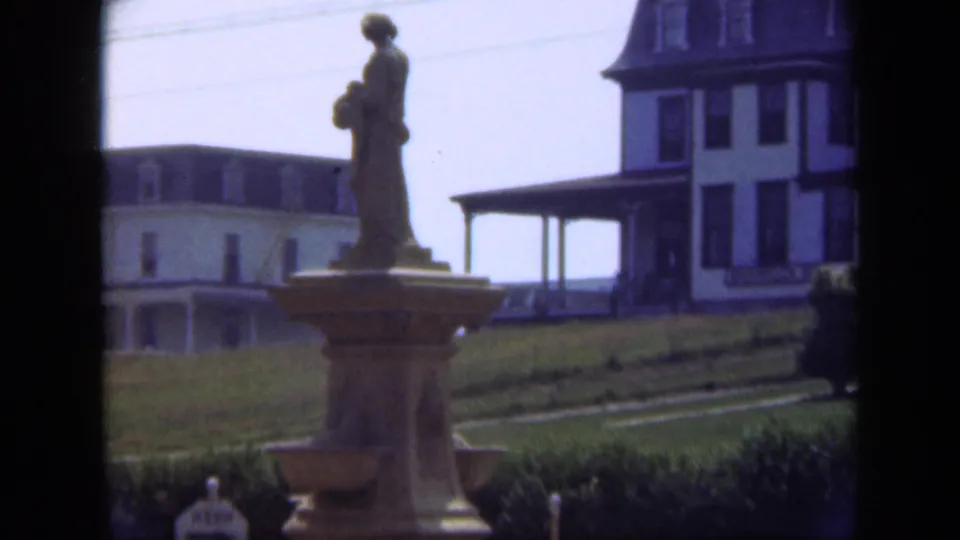 1948 Long Island exterior view with a statue on a pedestal, trimmed grounds, and a large building behind.