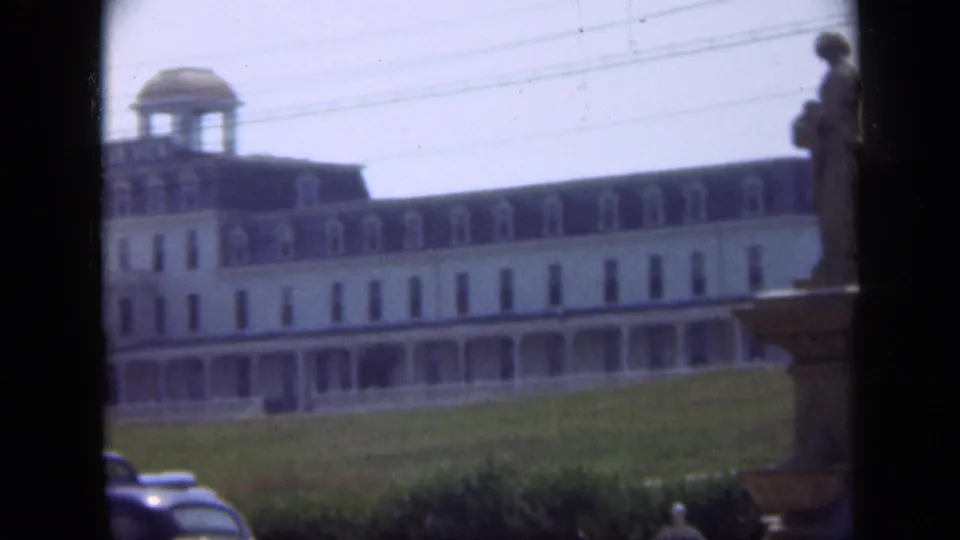 1948 Long Island frame showing a long cupola-topped building across a lawn, with a partial statue and cars near the lower edge.