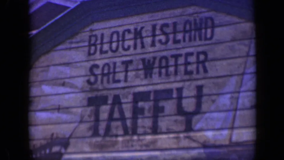 Close-up of a weathered wooden Block Island Salt Water Taffy sign in faded 8mm color with dark lettering.