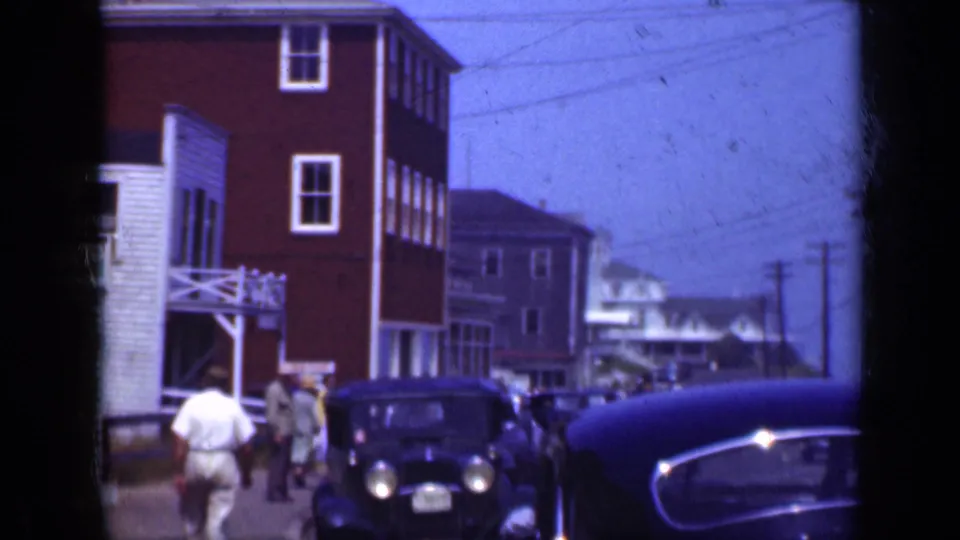 1948 Long Island street scene showing pedestrians, rounded parked automobiles, and storefront-style buildings near the water.
