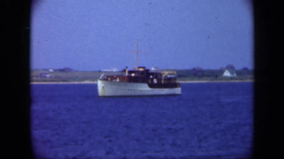 Small white motorboat on Long Island waters in 1948, with a low shoreline and distant houses behind it.