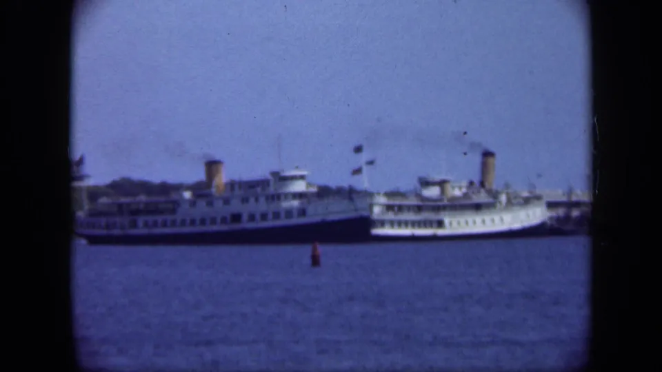A larger passenger ship or ferry appears offshore near Long Island, with a smaller vessel alongside and a buoy in the water.