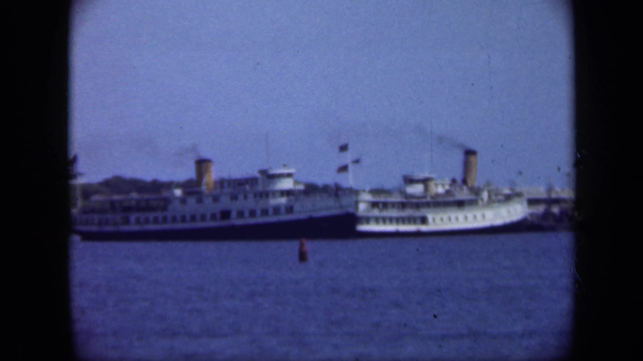 Two distant steamships docked across blue harbor water with dark 8mm frame edges.
