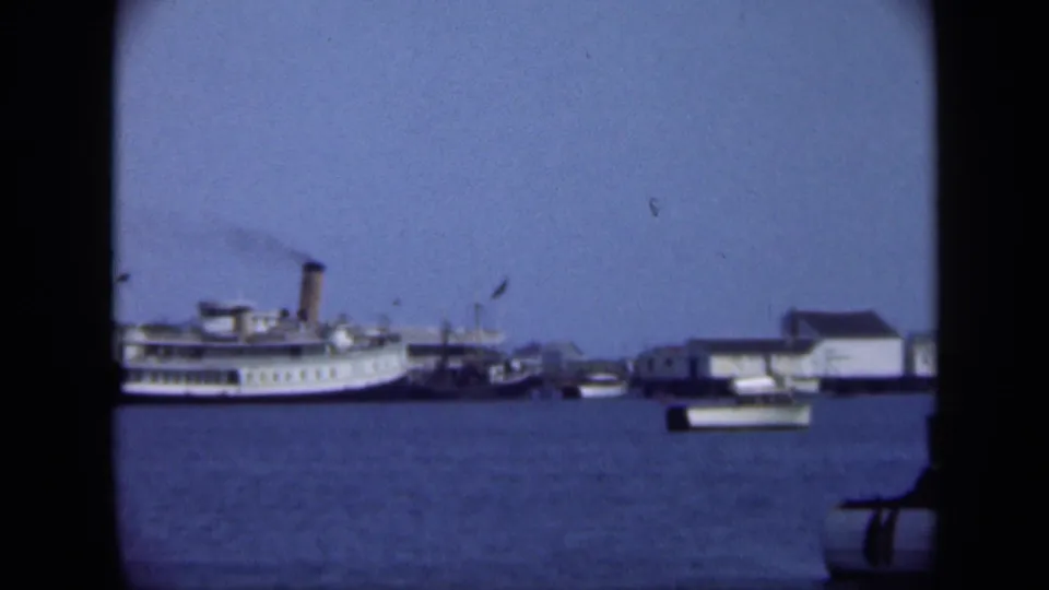 1948 Long Island waterfront view with a steamship partly at left, small boats, low buildings, and blue harbor water.