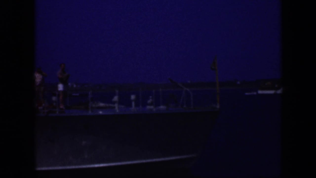 1948 Long Island 8mm frame showing a small passenger vessel in profile with deck railings and distant figures against a blue sky.