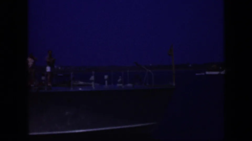 1948 Long Island 8mm frame showing a small passenger vessel in profile with deck railings and distant figures against a blue sky.