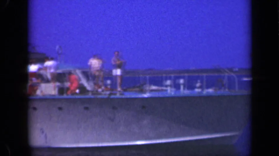 Passengers in summer clothing appear on the deck of a small Long Island boat, with railings and blue sky visible in the 8mm frame.