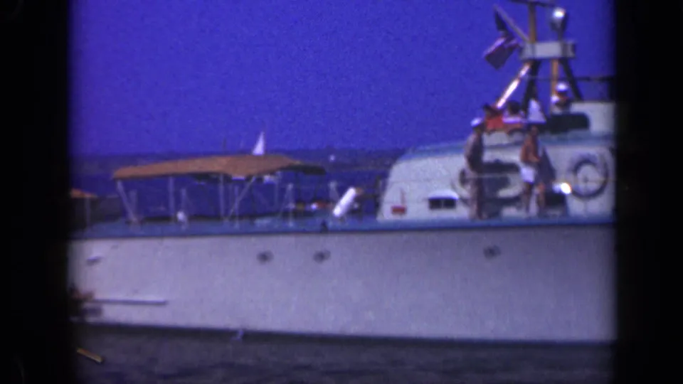 A 1948 Long Island 8mm frame shows the side of a white boat, a canopy, and two people near the cabin area.