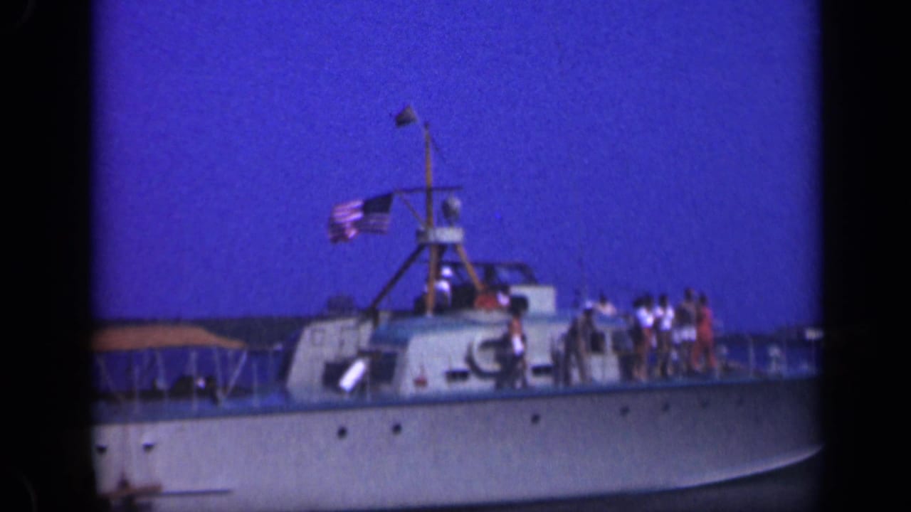 1948 Long Island home-movie frame showing a pleasure boat with passengers on deck, an American flag, canopy, and calm water.
