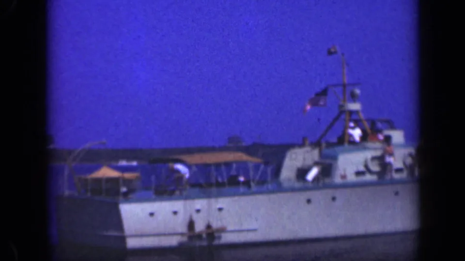 Home-movie frame of the stern section of a 1948 Long Island pleasure boat, showing canopy cover, American flag, mast, and passengers.