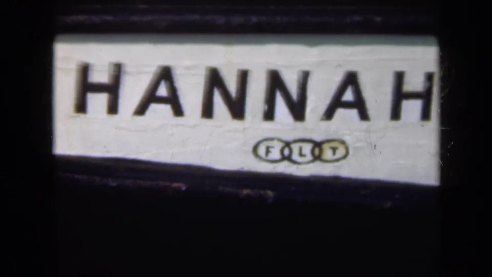 1948 Long Island 8mm frame showing a white sign with bold black HANNAH lettering and a small FLT mark beneath it.