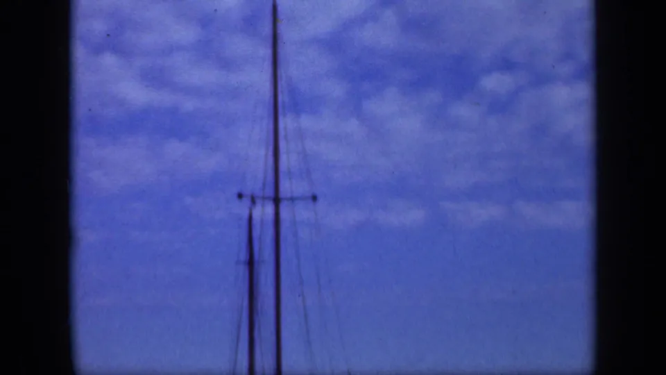1948 Long Island home-movie frame isolating the sailboat mast and rigging against blue sky and soft clouds.