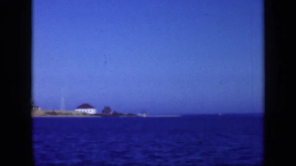 1948 Long Island waterfront frame showing a distant white shoreline building with a red roof beyond blue bay water.