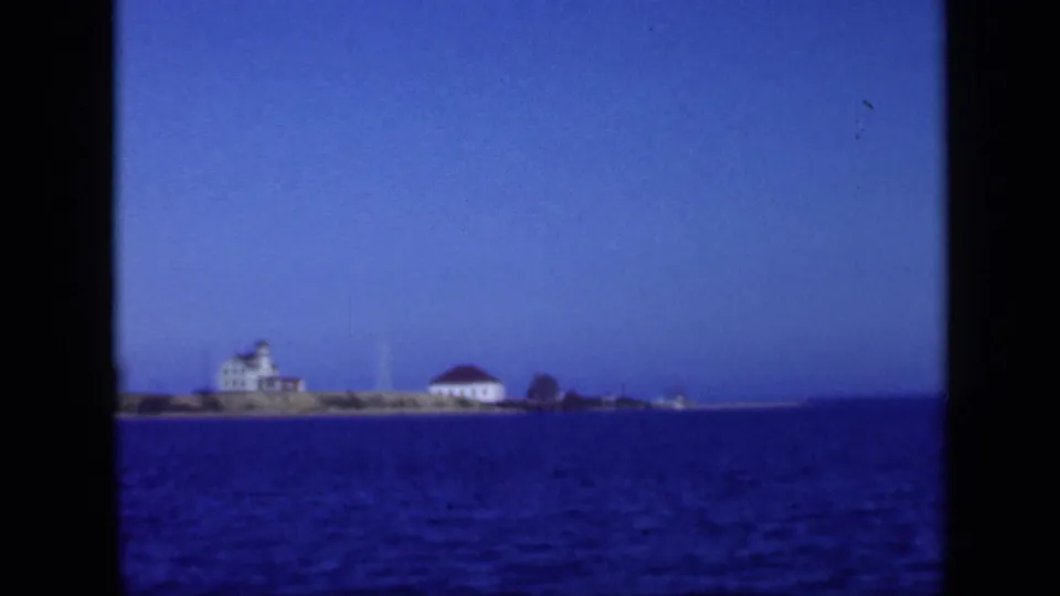 1948 Long Island bay pan frame with a white waterfront building, nearby red-roofed structure, blue water, and pale sky.