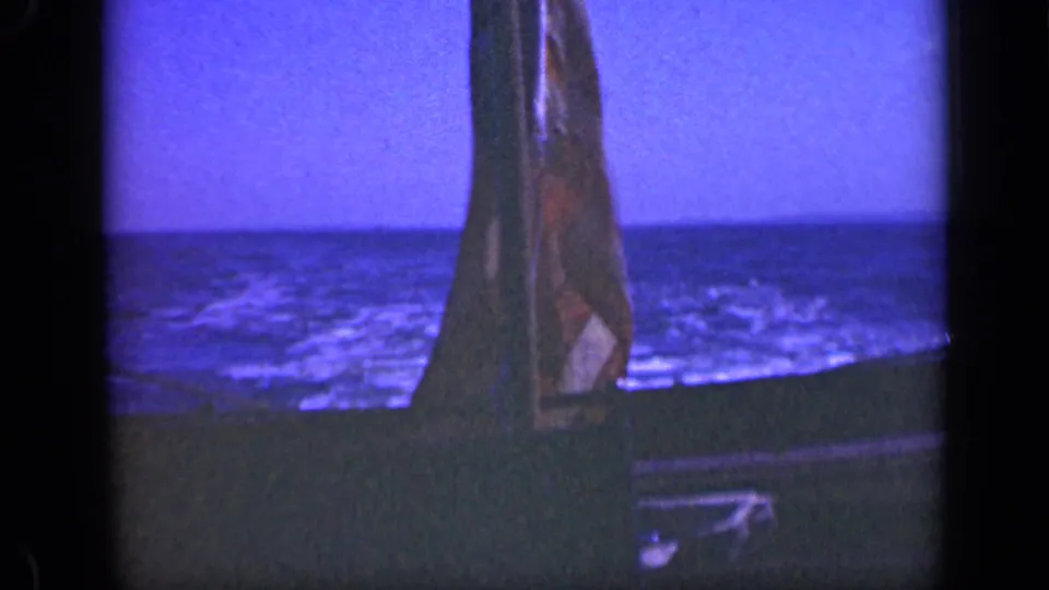 The flag remains centered near the boat edge as blue water stretches toward the horizon in the 1948 Long Island footage.