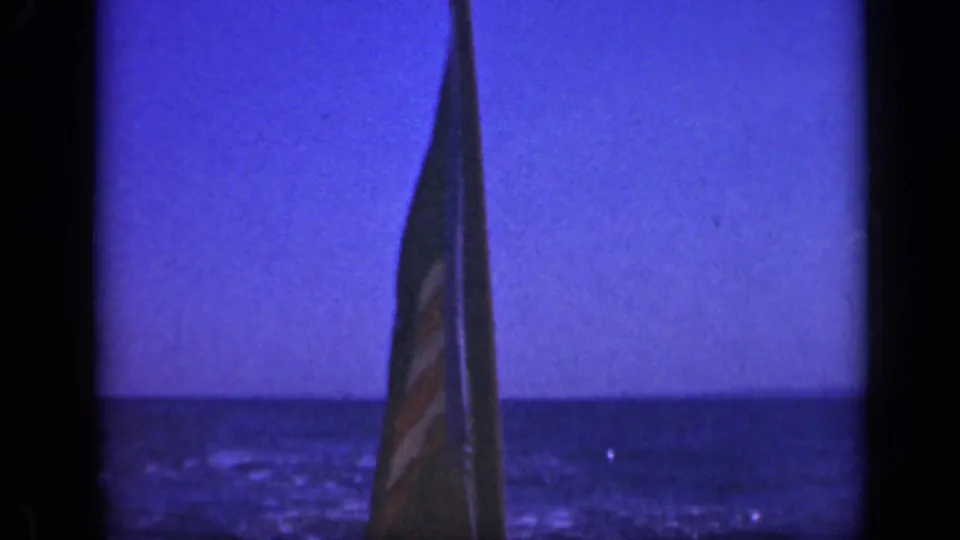 A close 8mm frame shows the flag wrapped partly around the pole above the water during the Long Island boat outing.