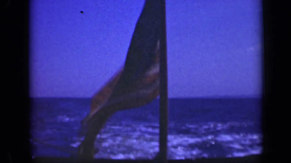 The American flag flutters across the pole as the 1948 Long Island home movie looks out over blue water.