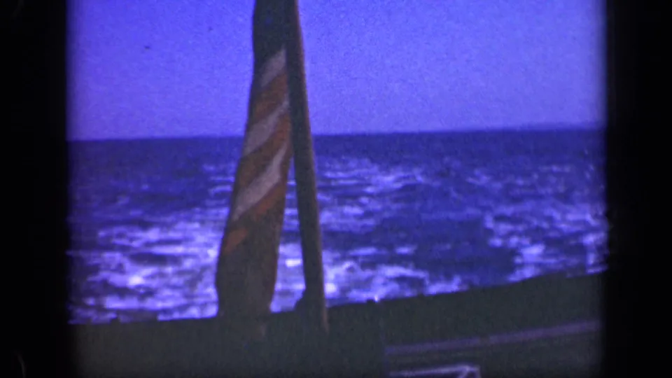 1948 Long Island home-movie frame with a partially visible U.S. flag, upright pole, boat edge, and choppy ocean beyond.
