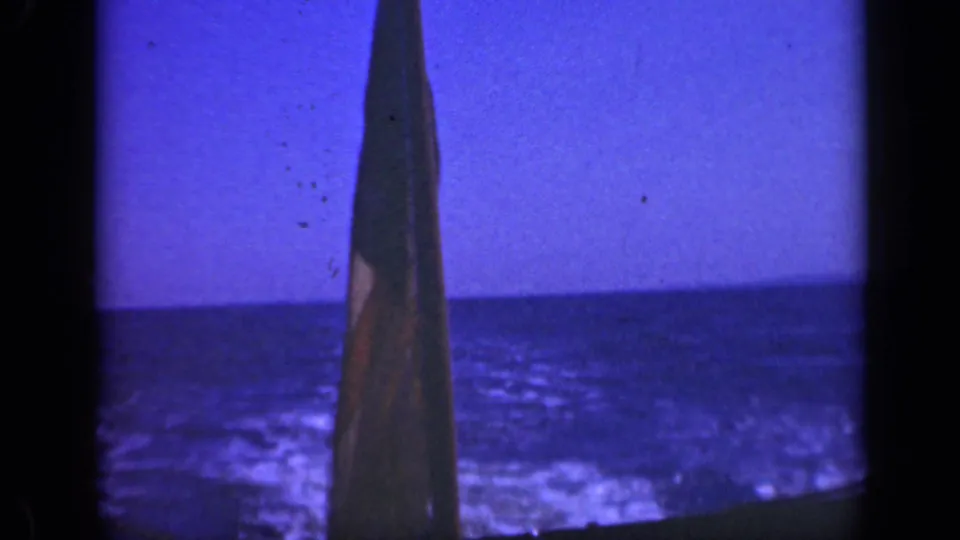1948 Long Island 8mm frame showing a close, vertical slice of flag fabric beside blue ocean and a straight horizon.