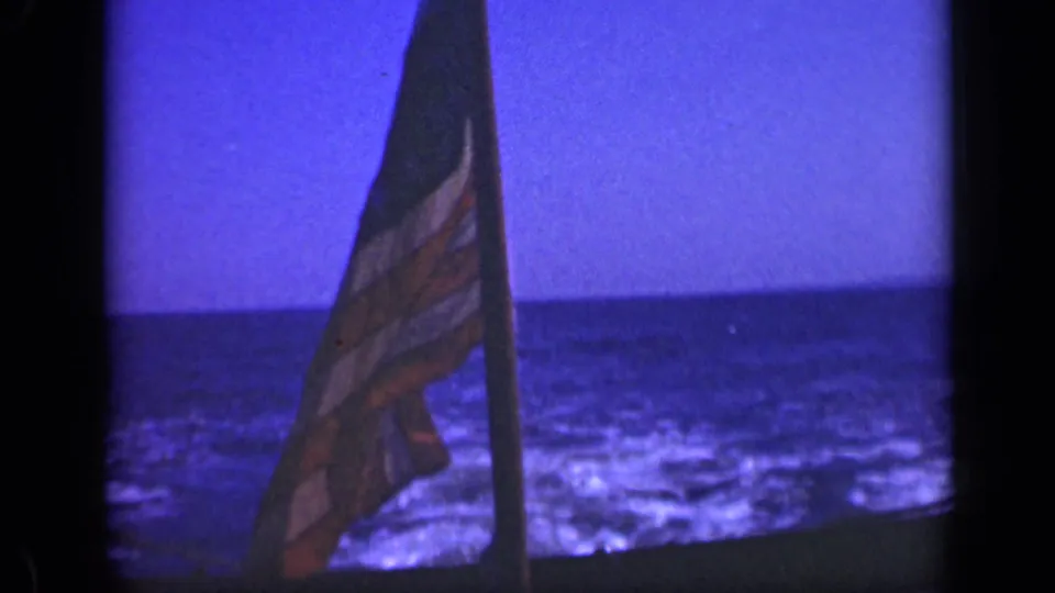 1948 Long Island home-movie frame with a U.S. flag hanging near rigging, set against blue water, wake, and horizon.