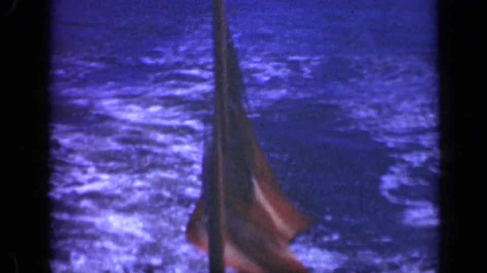 A partially framed U.S. flag hangs beside a ship mast over the blue sea in this 1948 home-movie frame.