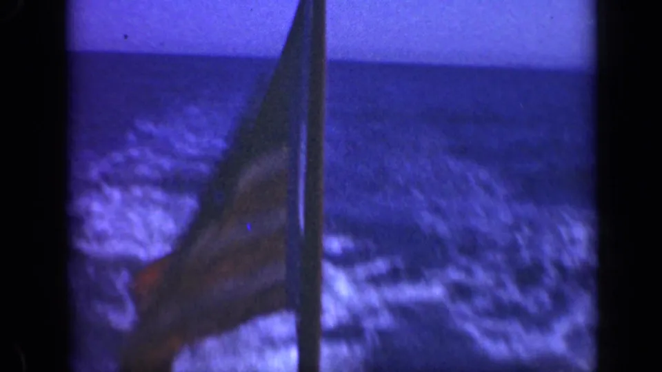 1948 8mm frame showing a U.S. flag beside a ship mast, with ocean horizon and blue sky visible.