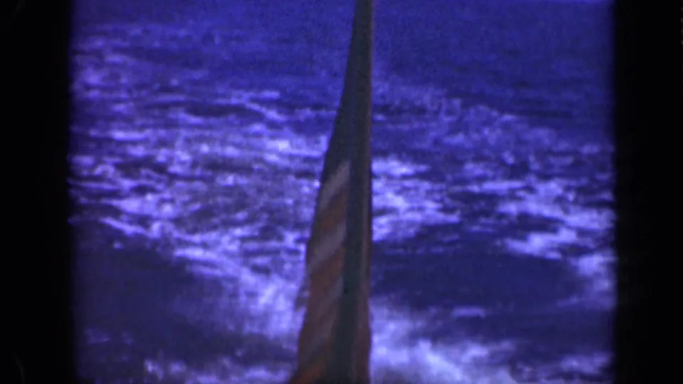 1948 8mm frame from off Long Island showing a U.S. flag beside a mast with dark rough ocean behind it.