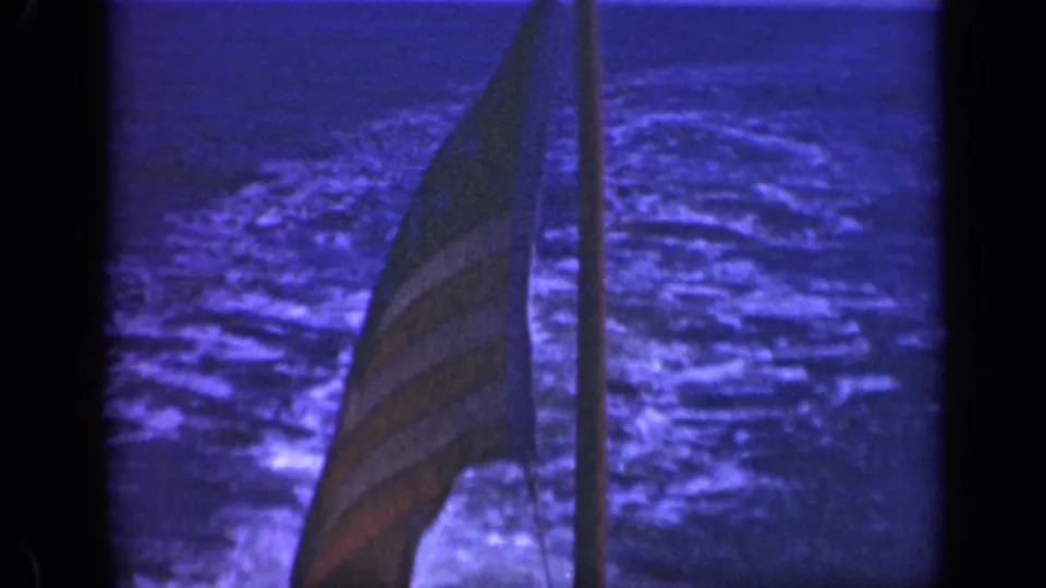 A U.S. flag on a vessel is seen near a vertical pole, with rough night water in the background.