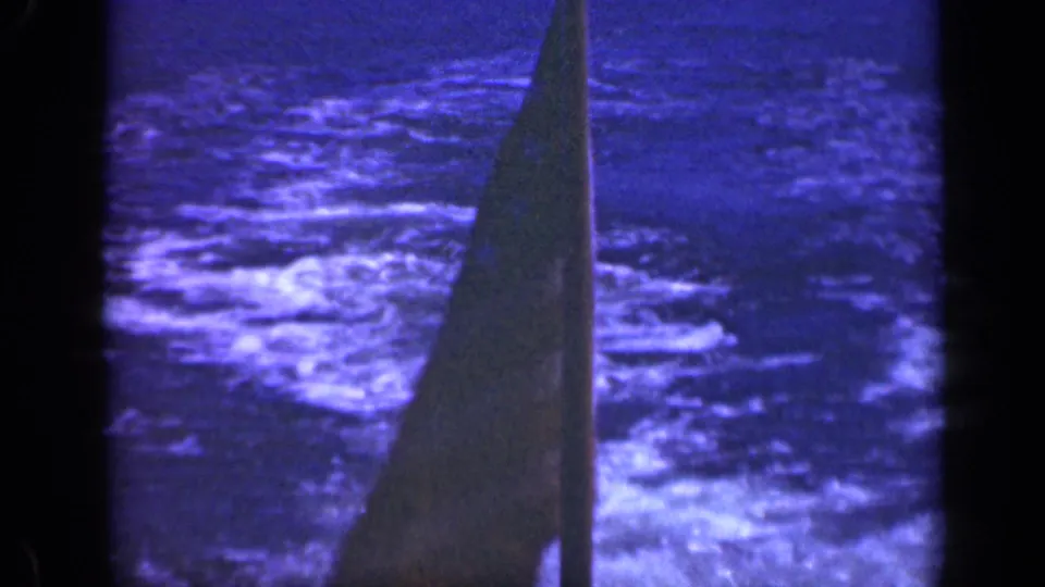 Low-light 8mm view of the flag and mast area, with rough ocean surface visible behind it.