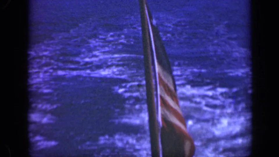 A striped U.S. flag appears along the right side of the frame over blue-toned choppy water.