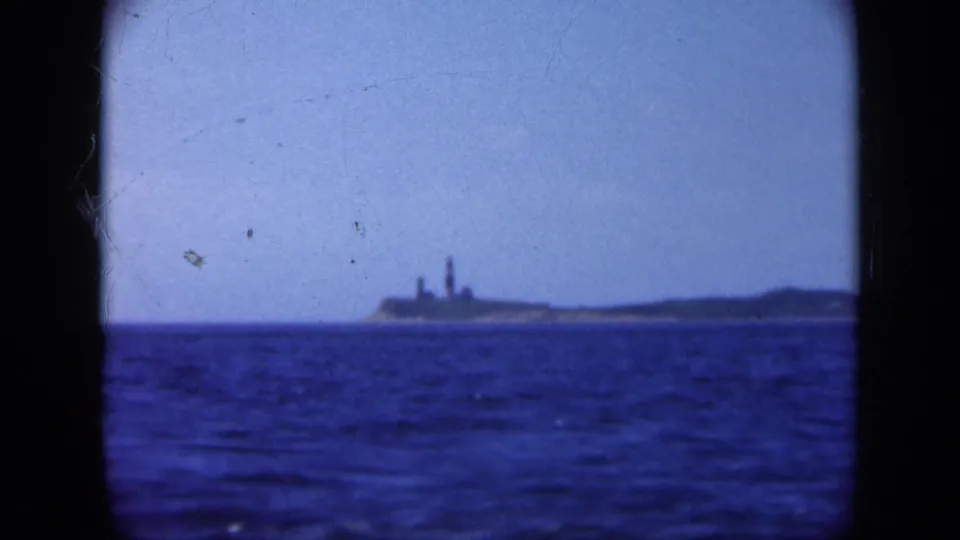 Distant Long Island coastal structure, possibly a lighthouse, seen across blue water in a 1948 home-movie frame.