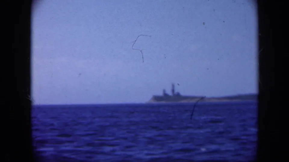 Soft 8mm view of a distant Long Island cape with a lighthouse-like tower and adjacent structures across the water.