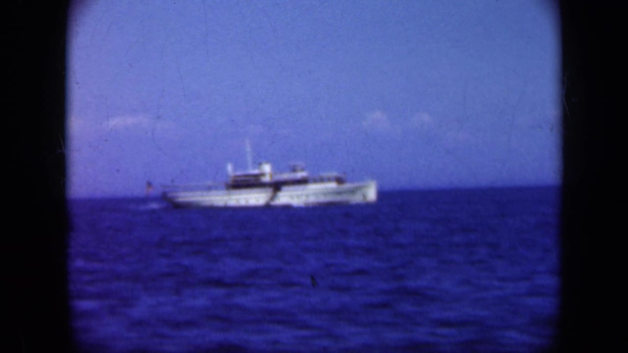 White passenger ship on blue water under a clear sky, framed by black film borders.