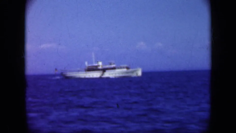 1948 Long Island 8mm frame showing a white passenger ship crossing deep blue water beneath a clear horizon.