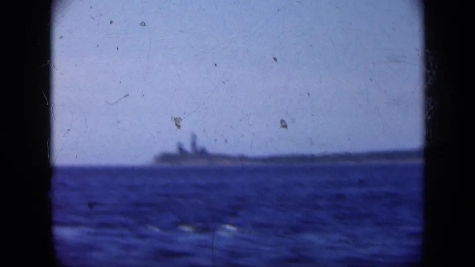 Distant Long Island shoreline or island appears on the horizon beyond blue water in a 1948 8mm frame.