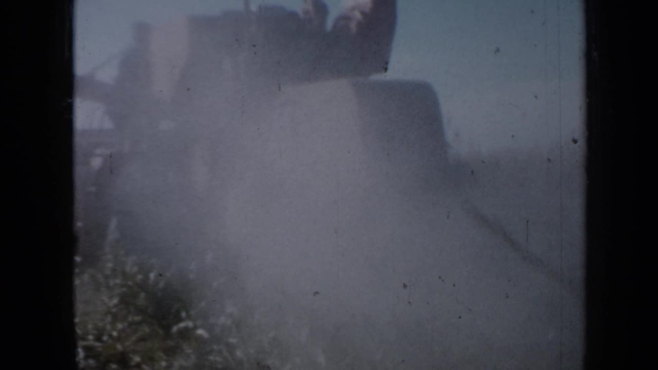 Dust surrounds a large harvester moving through a field.