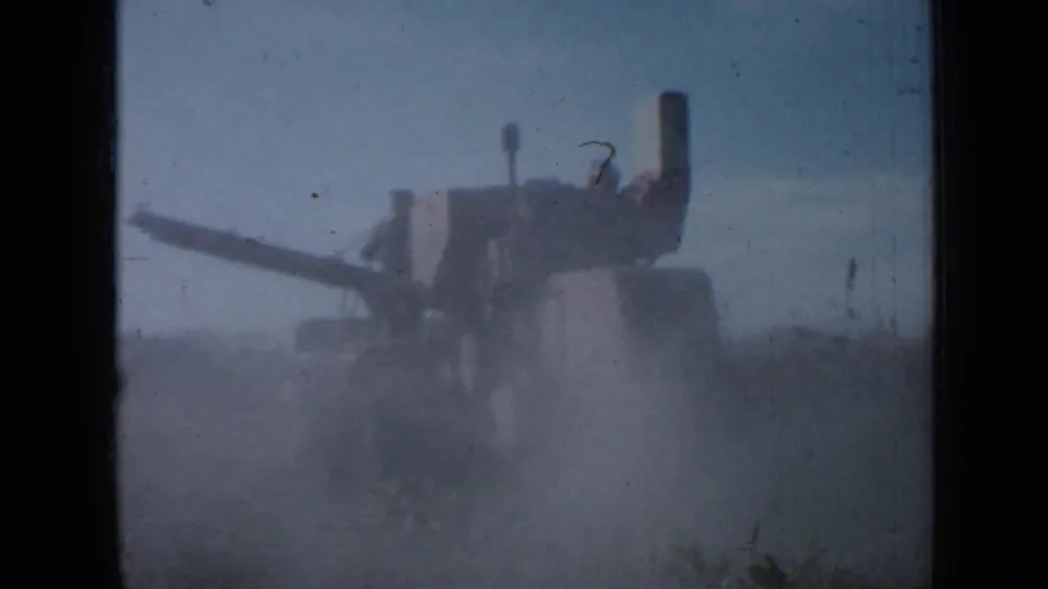 The 1958 Minnesota harvester is seen in profile through dust, with the auger stretched across the frame over the crop.