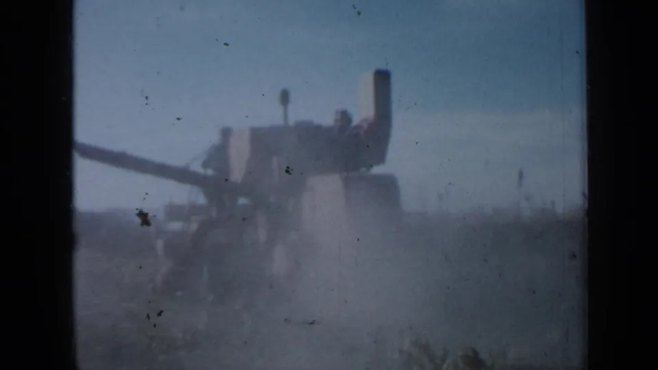 1958 Minnesota 8mm frame showing a distant tractor or harvester working through tall crops under a hazy sky.
