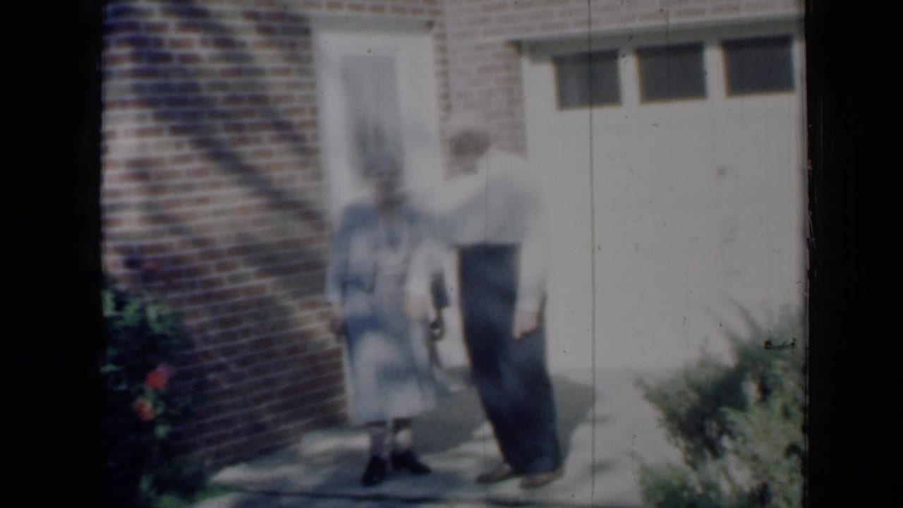 Elderly couple standing outside a brick house near a pale door.