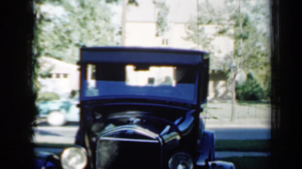 A black vintage car appears parked along a residential street in the same 1958 Minnesota home-movie sequence.