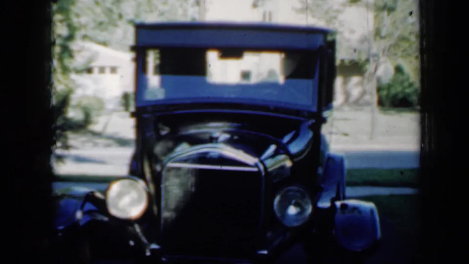 1958 Minnesota frame with the antique car more centered, its tall windshield, rounded headlights, grille, driveway, and background house visible.
