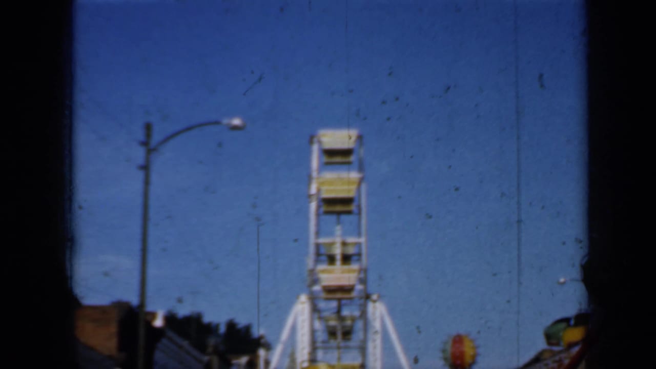 White Ferris wheel behind dark film-frame edges under a blue sky.