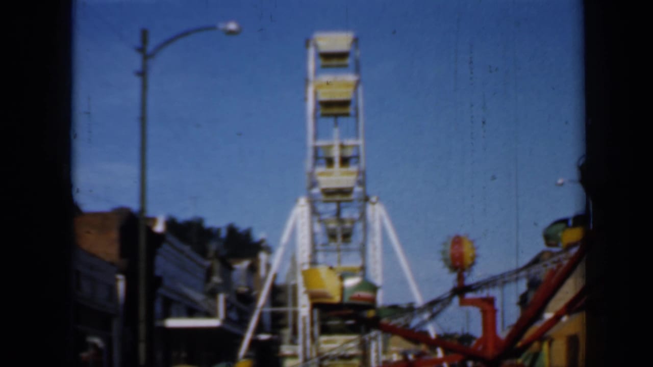 Ferris wheel and red carnival ride visible beside storefronts.