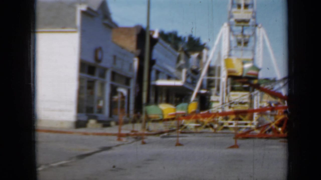 Portable amusement rides appear set up along a Minnesota town street in 1958, with storefronts visible nearby.
