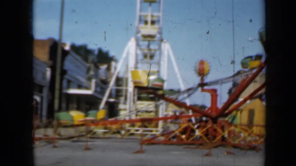 1958 Minnesota frame with a white Ferris wheel, red spinning ride arms, and town buildings in soft 8mm color.