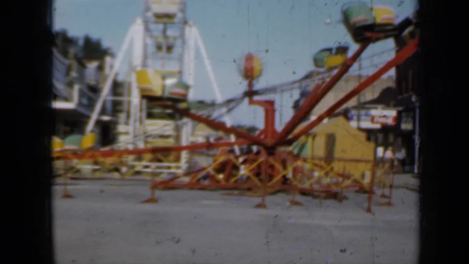 1958 Minnesota 8mm frame showing a stationary red and yellow carnival ride with a white Ferris wheel rising behind it.