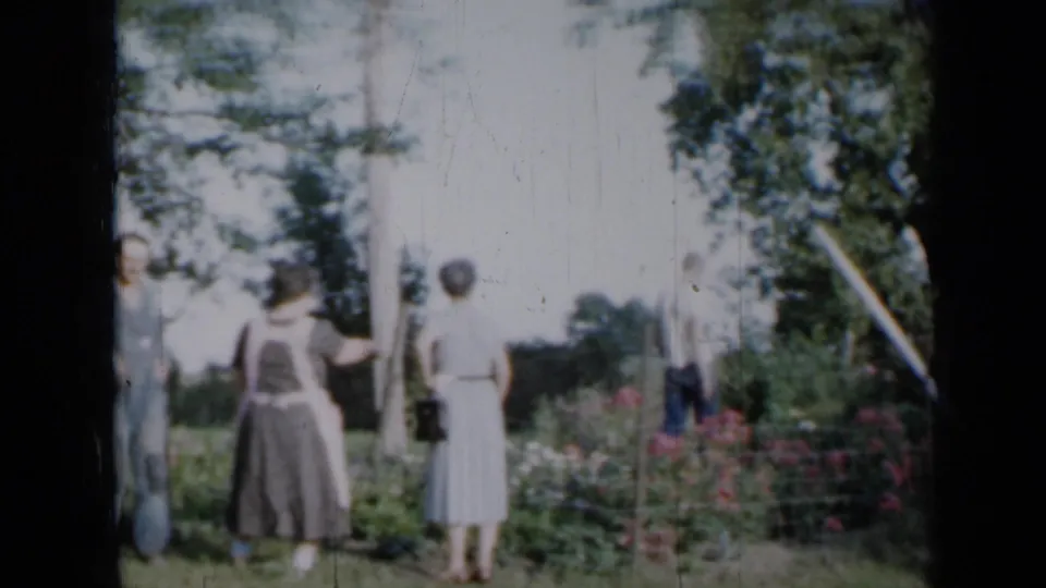 The man has moved toward the edge of the frame while two women remain beside the fenced flower bed in the metadata-supported Minnesota garden scene.
