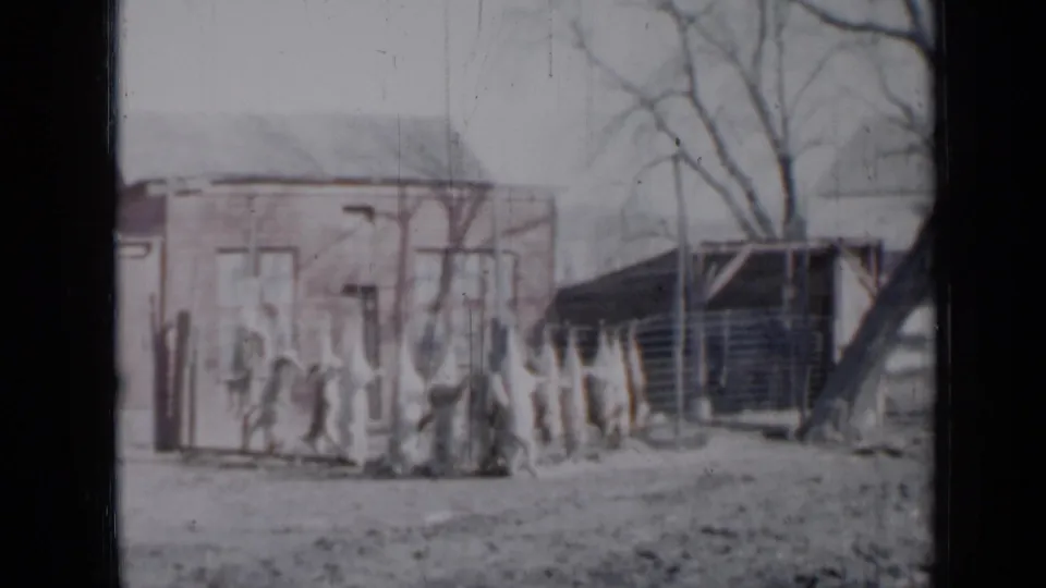 1958 Minnesota 8mm frame showing two small suburban houses, a fence, bare trees, and faint people near the yard edge.