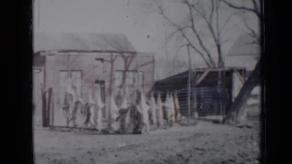 1958 Minnesota 8mm view of a backyard with two modest houses, a fence line, bare trees, and indistinct people by the fence.